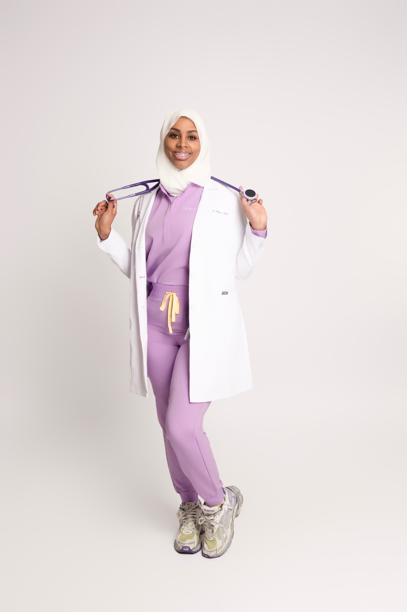 Ny’Rossha Alim in purple scrubs and a white coat, holding a stethoscope